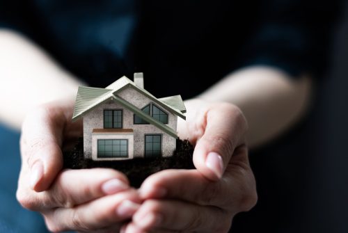 Model house in woman's hand, boxes in the background.